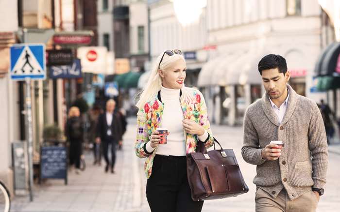 Kvinna och man promenerar på stan med take away kaffe i handen
