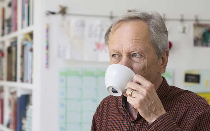 Äldre man dricker kaffe ur vit kopp
