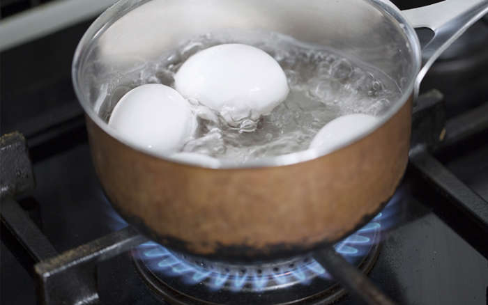Kastrull med tre ägg som kokar på gasspis