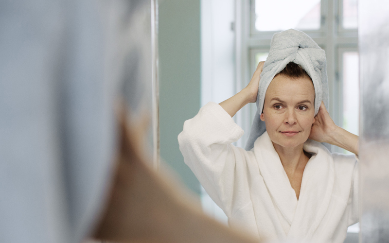 Kvinna i badrum med vit handduk om håret